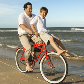 dad riding bike with his son on the beach